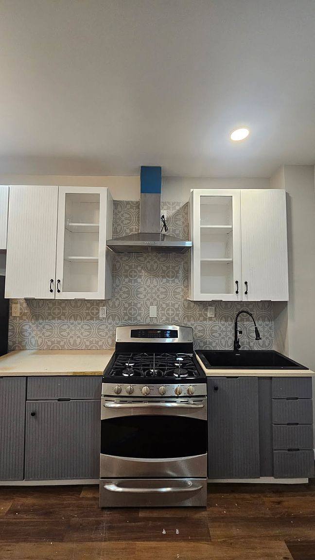 Kitchen with gray lower and white upper cabinets, a stainless GE range and a range hood