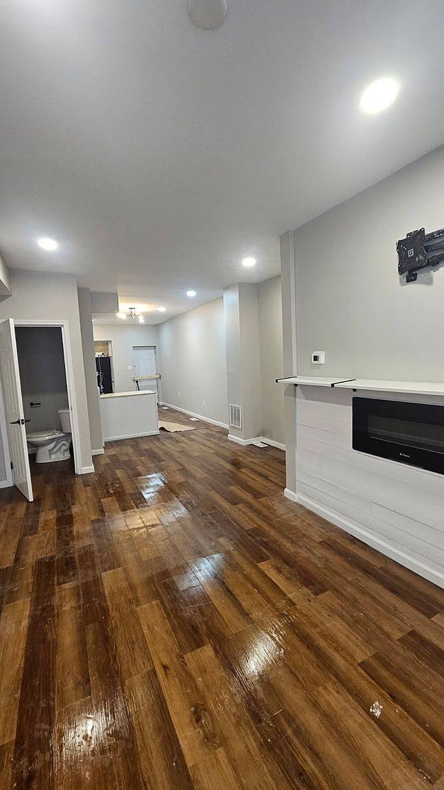 Living room with wood-look floors, recessed lights and a wall-mounted electric fireplace