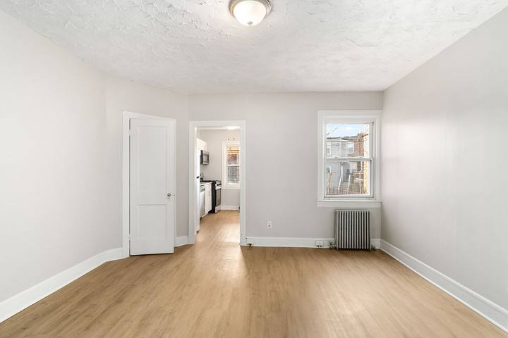 Living room with plank floors, a radiator under the window and an arched opening to the dining room