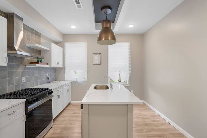 Kitchen with white shaker cabinets, gray tile backsplash, a gas range and a center island