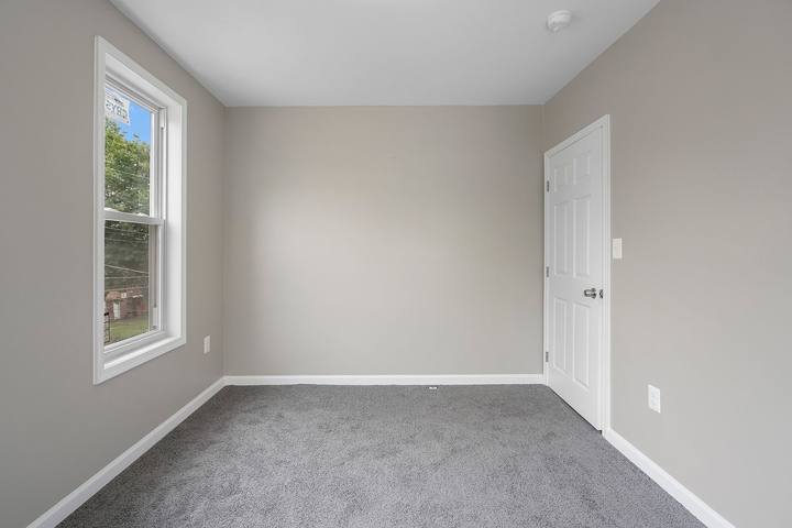 Carpeted bedroom with a window, fresh gray paint and a white door
