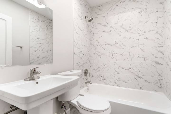 Bathroom with marble-look tile around the tub and a pedestal sink